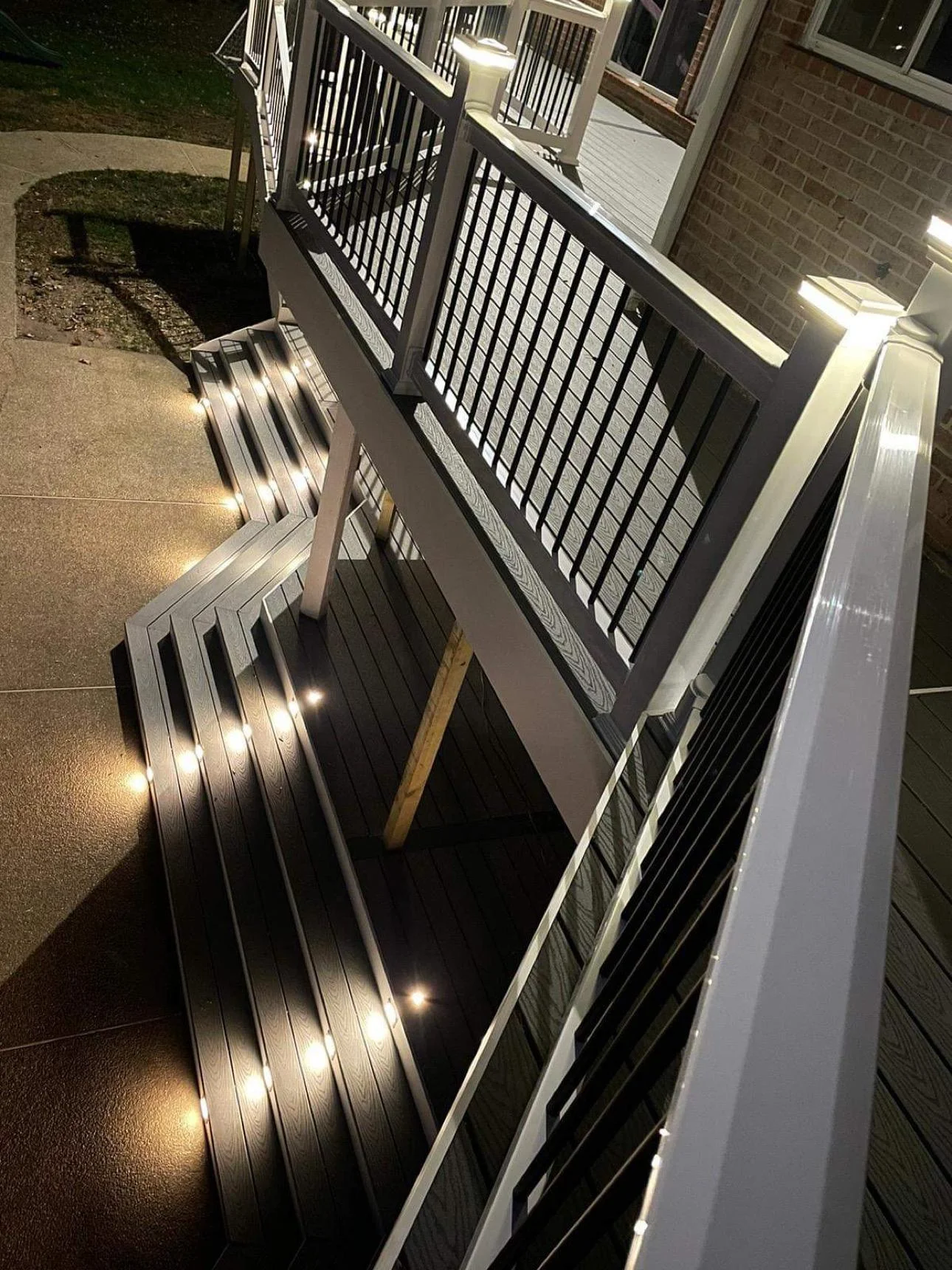 Multi-tier deck replacement Everett WA staircase Close-Up Of Deck Railing With Dark Vertical Balusters, Light-Colored Posts, And Illuminated Steps Below