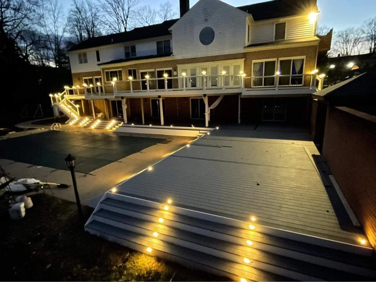 Luxury poolside deck replacement Everett WA at dusk Backyard Overview With An Elevated Deck, Poolside Decking, And Illuminated Steps At Dusk In Everett