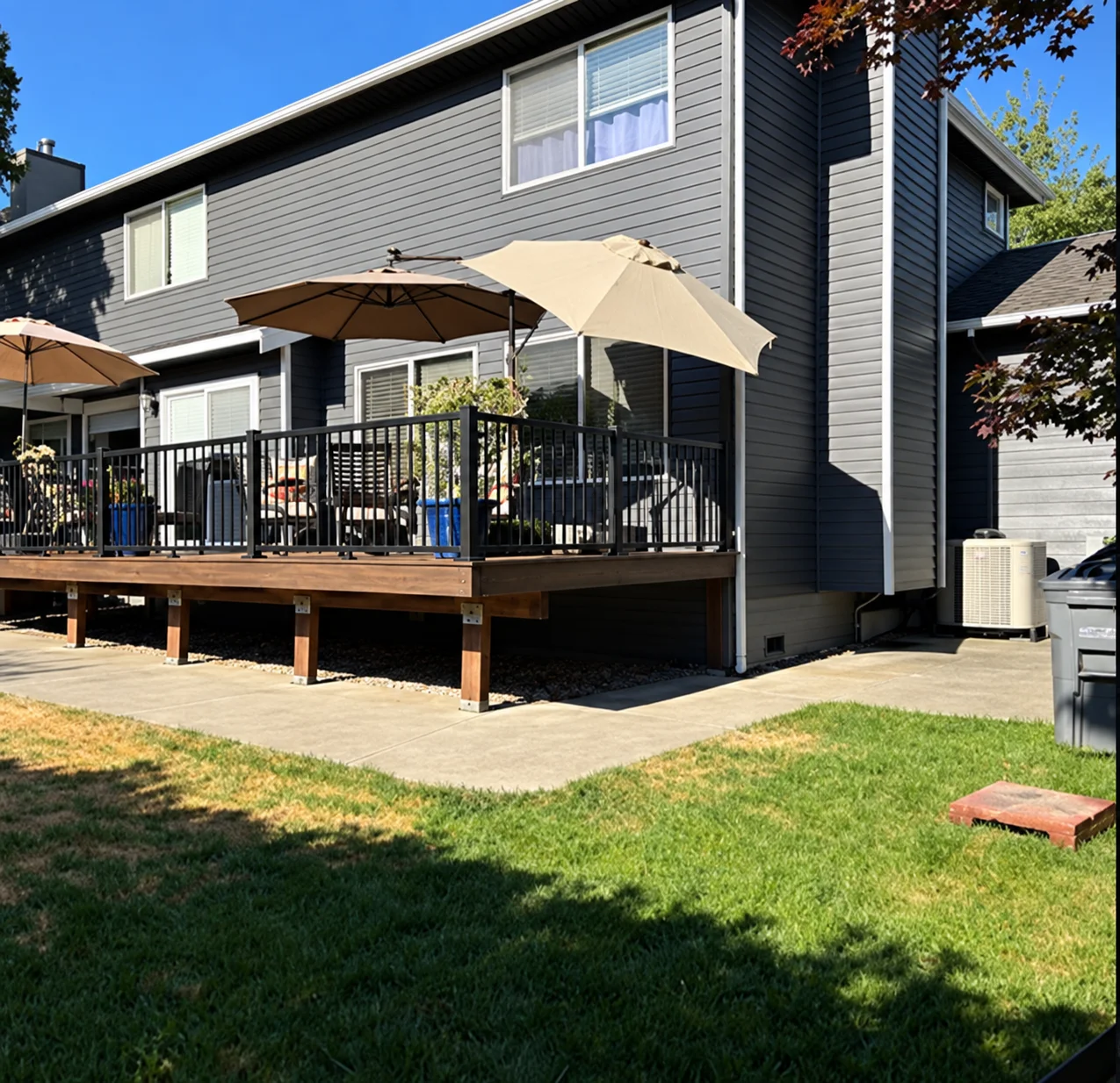 Elevated backyard composite patio area highlighting a Trex Transcend deck replacement in Bothell. Finished Trex Transcend Deck With Staircase And Cable Railing Beside A Bothell Home In Washington