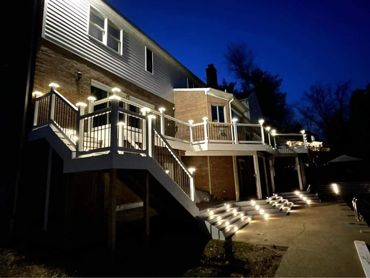 Custom deck replacement Everett WA with illuminated railings Raised Backyard Deck With Illuminated Railing Posts And Stairs Viewed From Ground Level At Dusk
